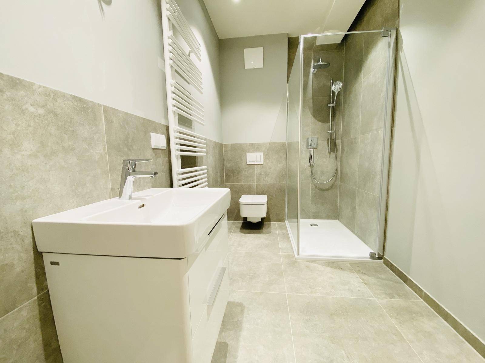 Modernes Badezimmer mit Dusche, Waschbecken, WC und beheiztem Handtuchhalter.