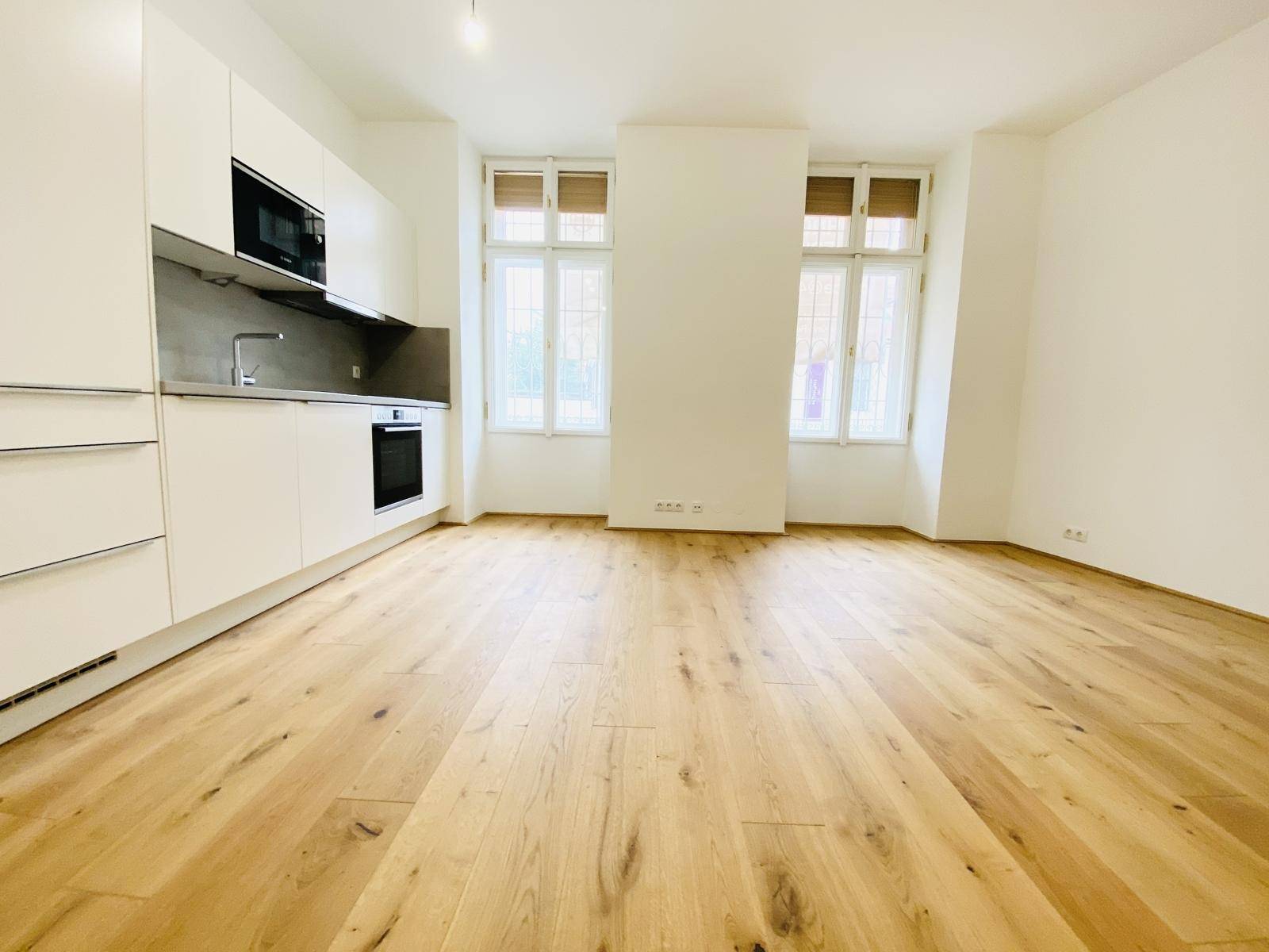 Heller Wohnbereich mit integrierter Küchenzeile und Holzboden, gut beleuchtet.