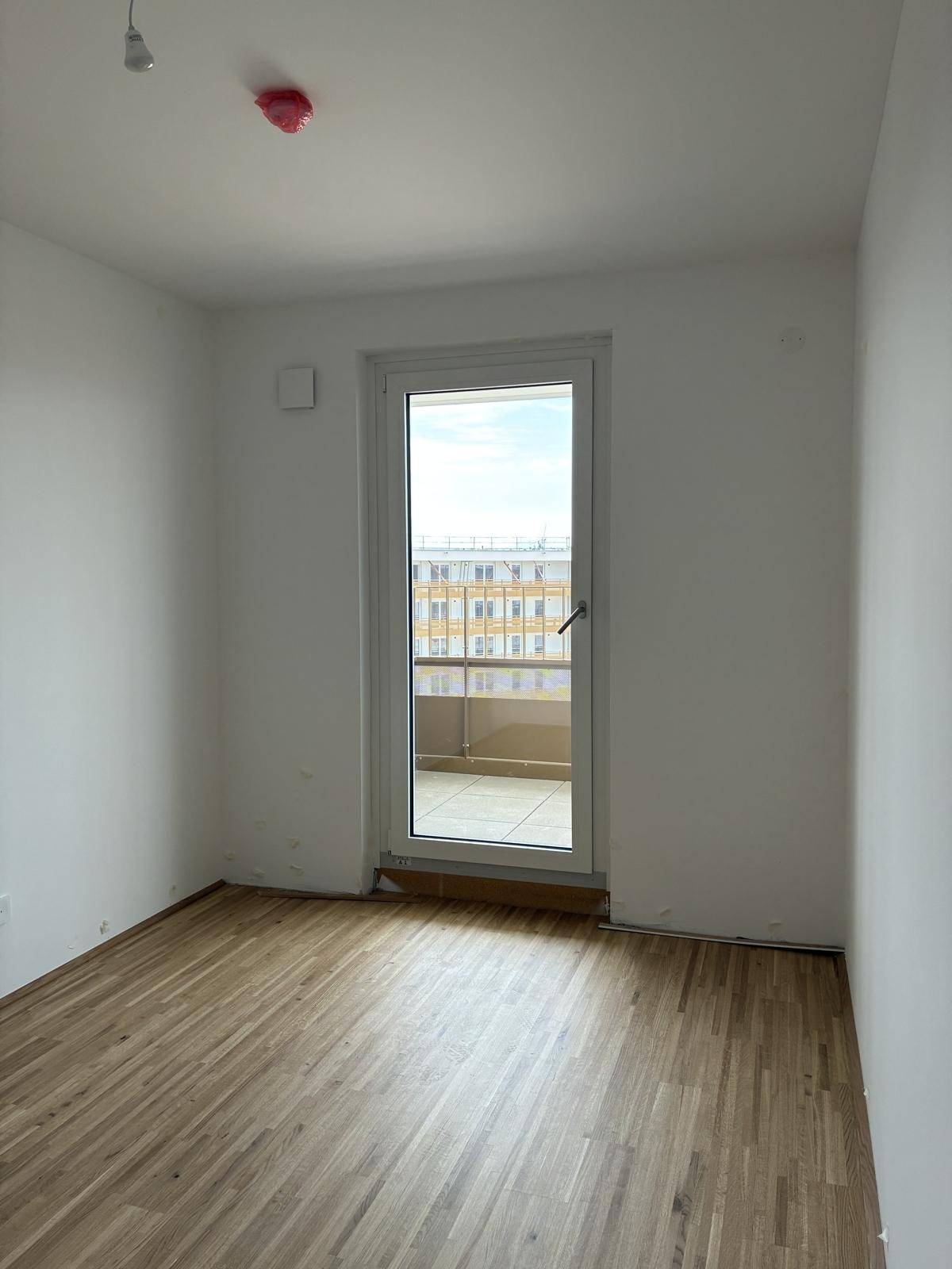 Kleineres Zimmer mit Holzboden und Zugang zu einem Balkon durch eine einzelne Tür.