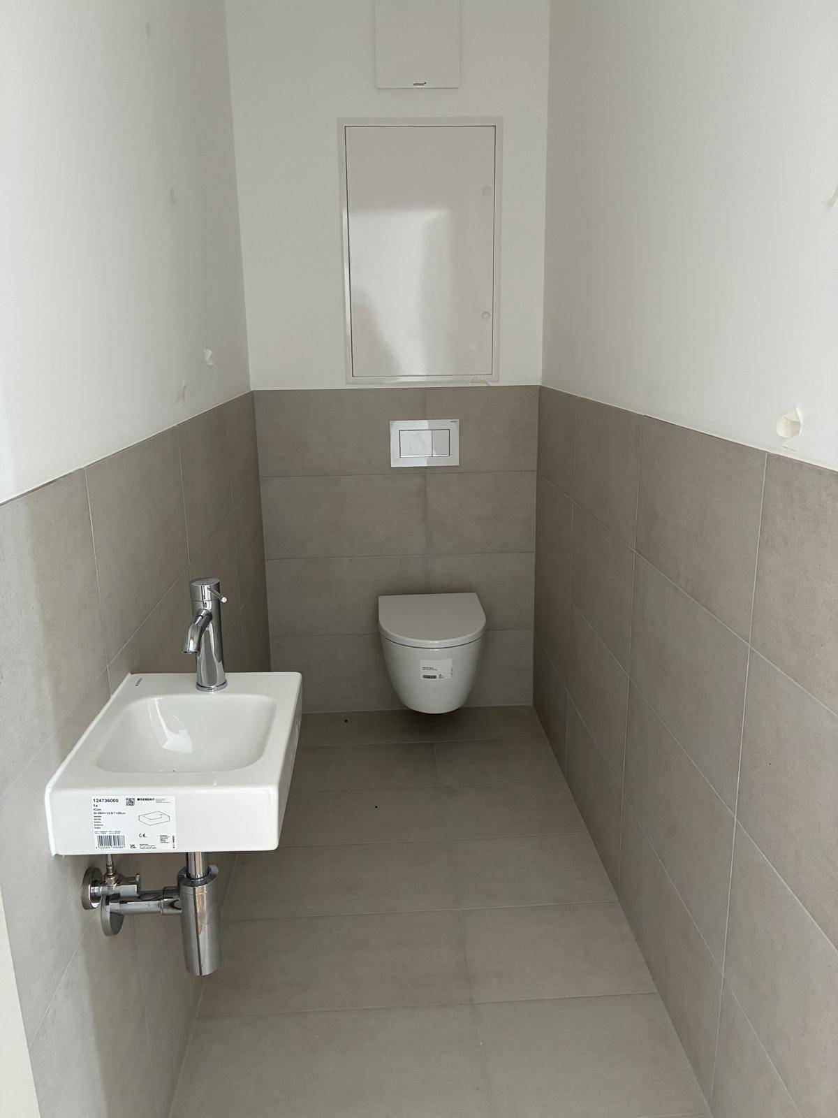 Gäste-WC mit hellgrauen Fliesen, wandhängendem WC und kleinem Handwaschbecken im modernen Stil.