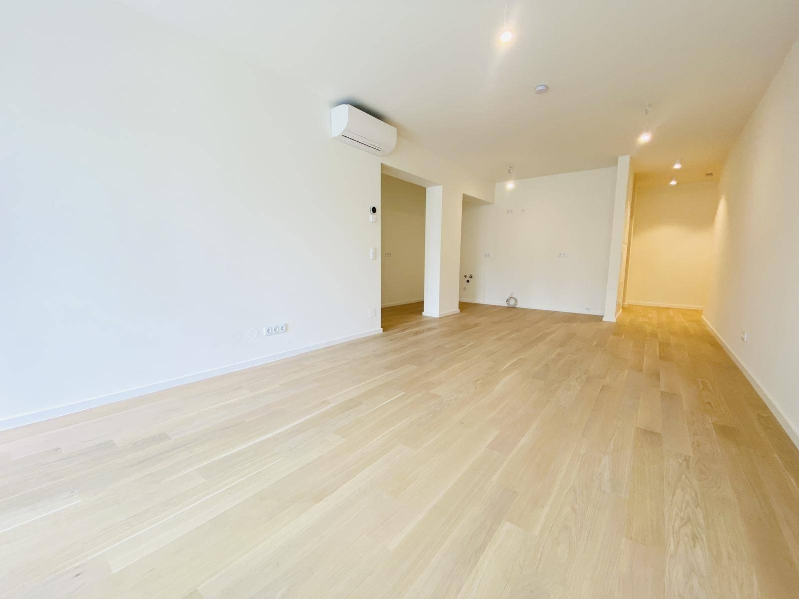 Geräumiges, leeres Wohnzimmer mit hellem Parkettboden und installierter Klimaanlage.