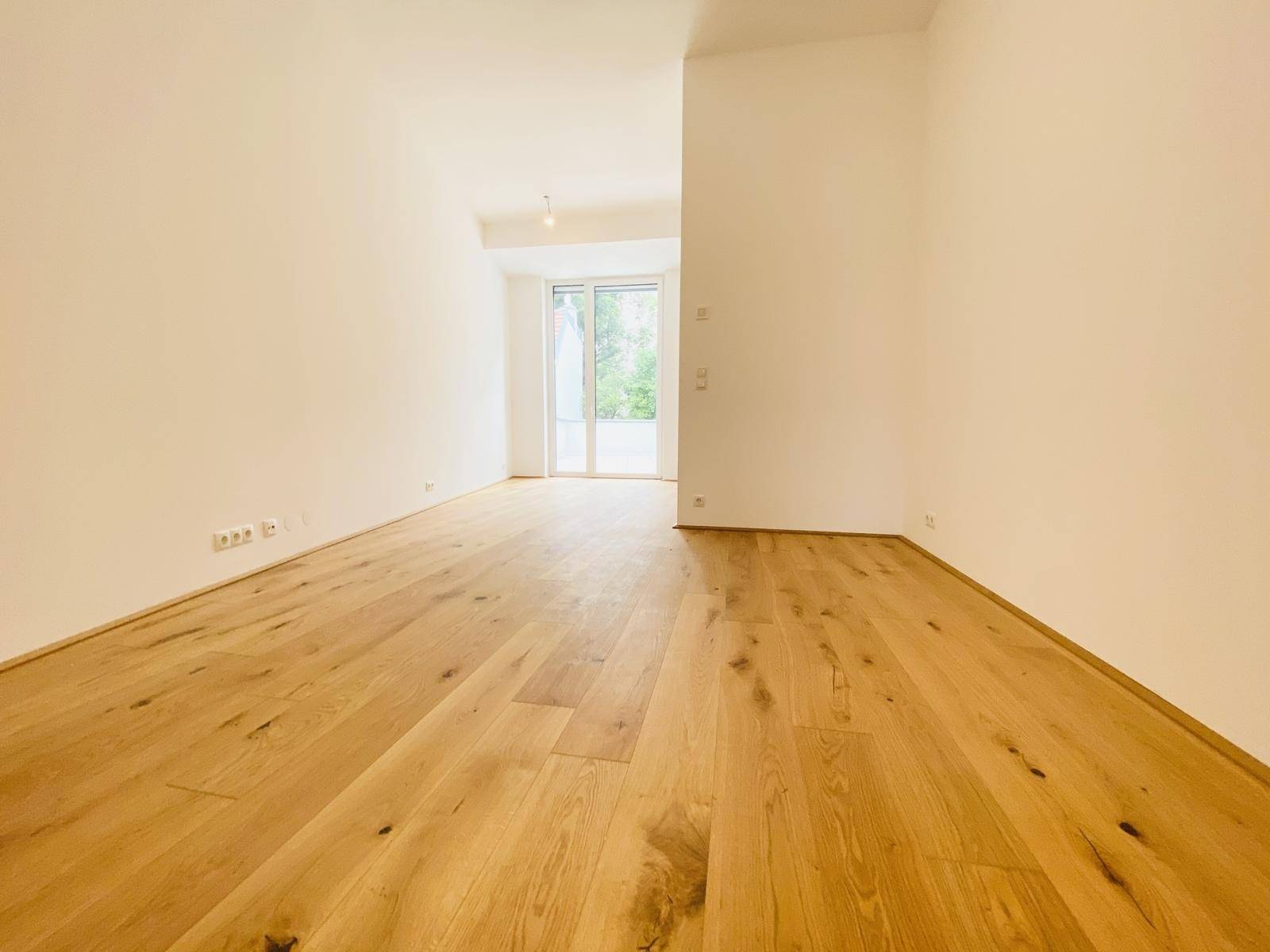 Lichtdurchfluteter Wohnraum mit Holzboden und großen Fenstertüren zum Außenbereich.