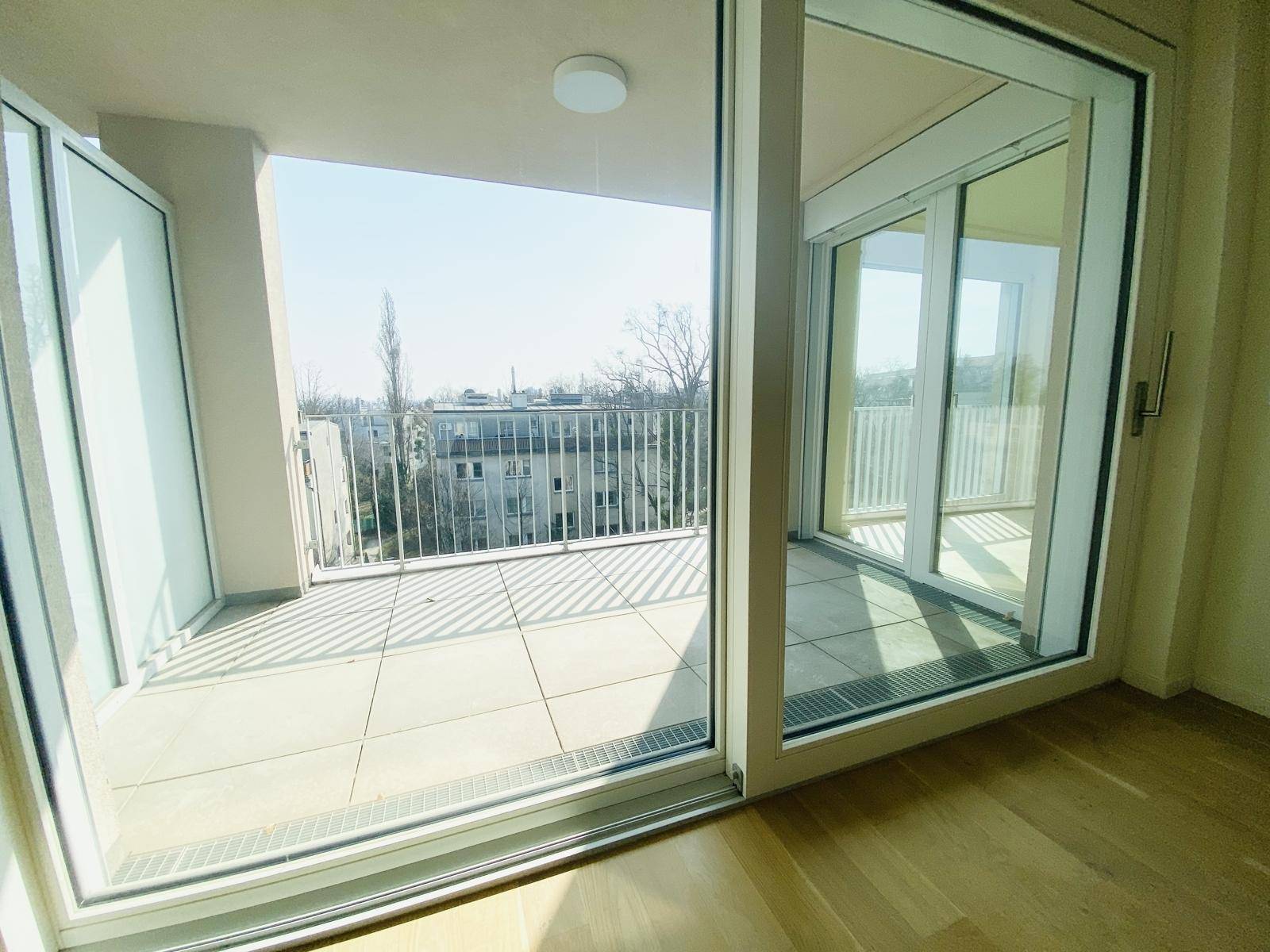 Heller Wohnraum mit großen Schiebetüren, die auf einen sonnigen Balkon führen.