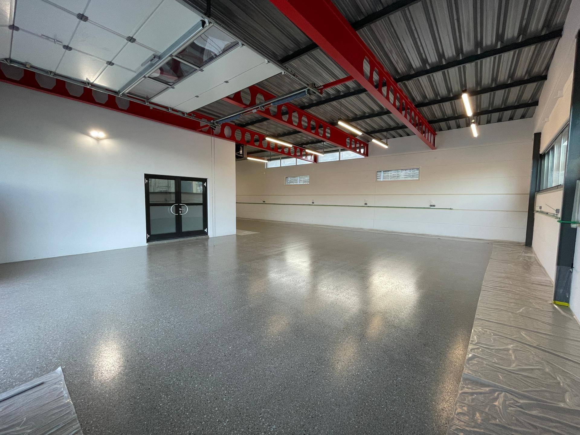 Große, helle Lagerhalle mit roter Stahlkonstruktion, hohen Decken und glänzendem Boden.