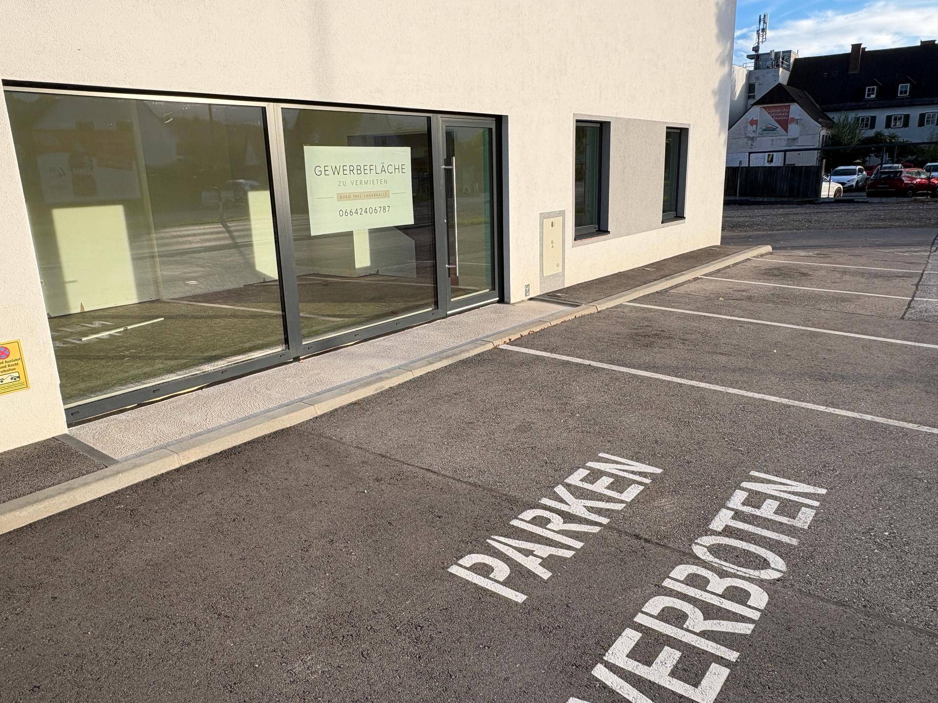 Eingangsbereich des Gewerbeobjekts mit großen Glasfenstern und markierten Parkplätzen.