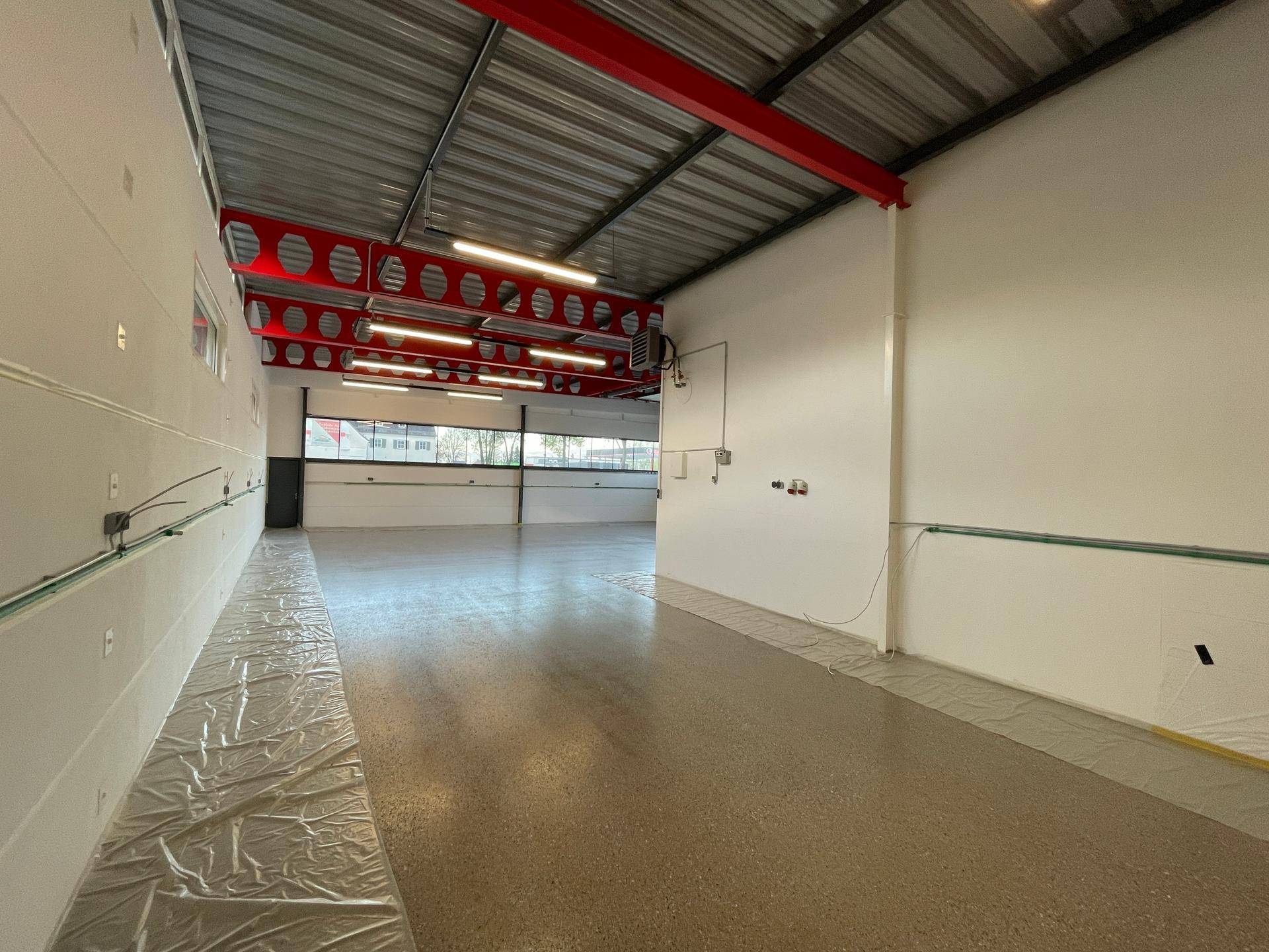 Geräumige Lagerhalle mit Industrieboden, roter Stahlkonstruktion und viel Tageslicht.