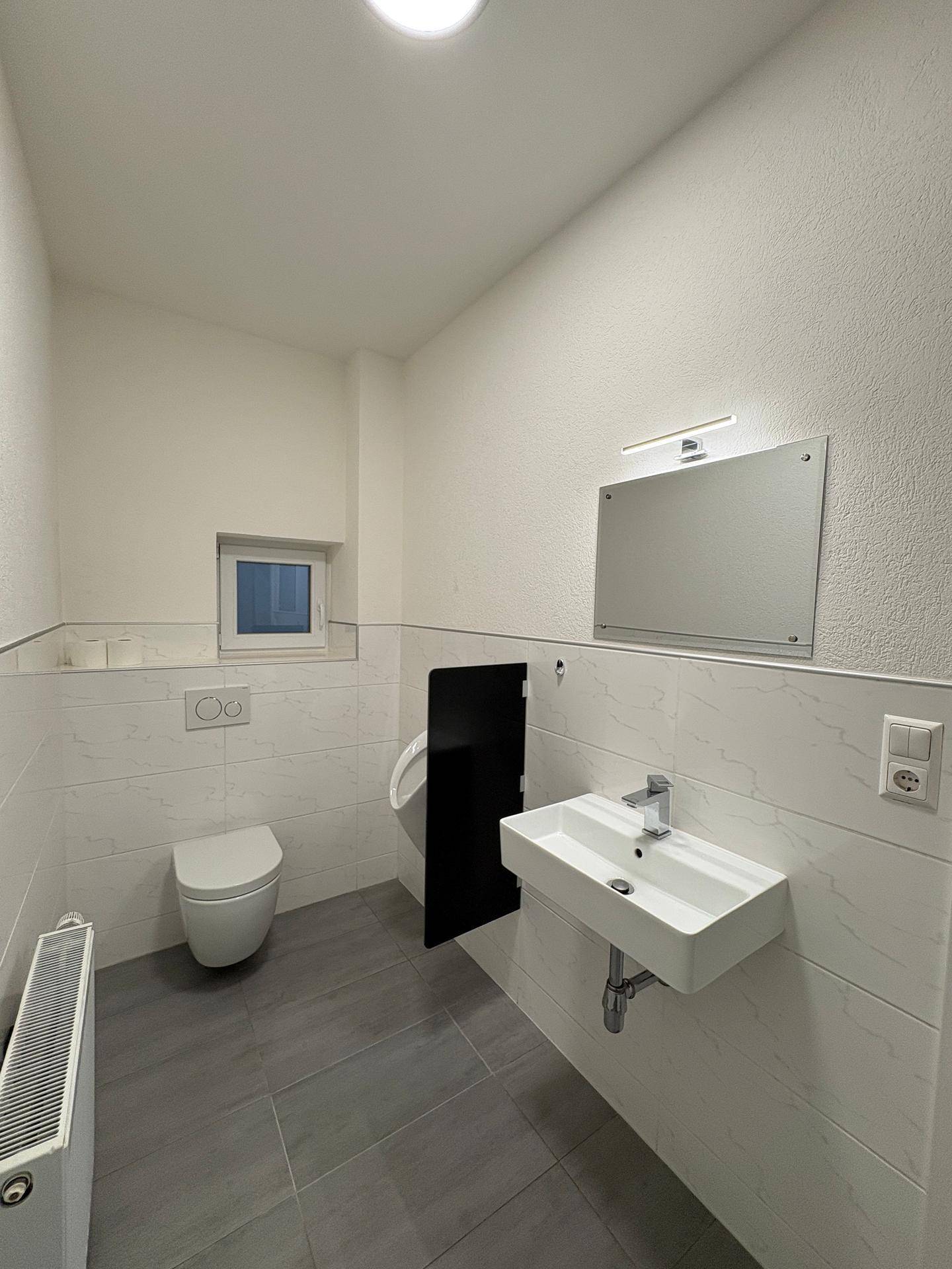 Modernes Gäste-WC mit wandhängender Toilette, Urinal, Waschbecken und Fenster.
