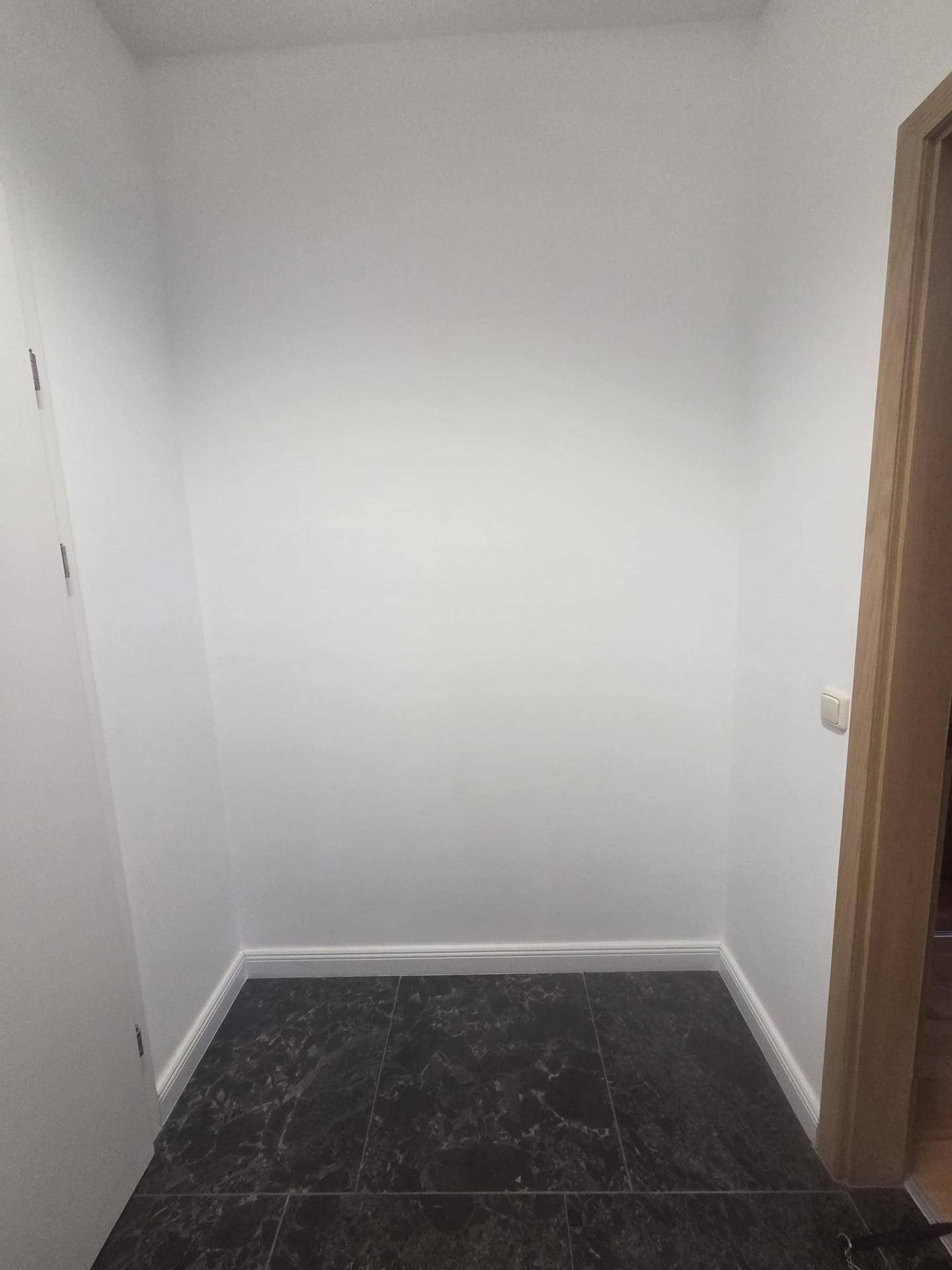 Kleiner Bereich im Flur mit dunklem Fliesenboden und weißen Wänden.