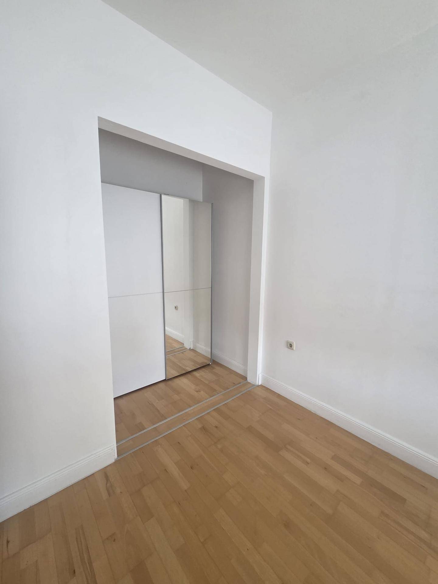 Leeres Zimmer mit Holzboden und einem eingebauten Spiegelschrank.
