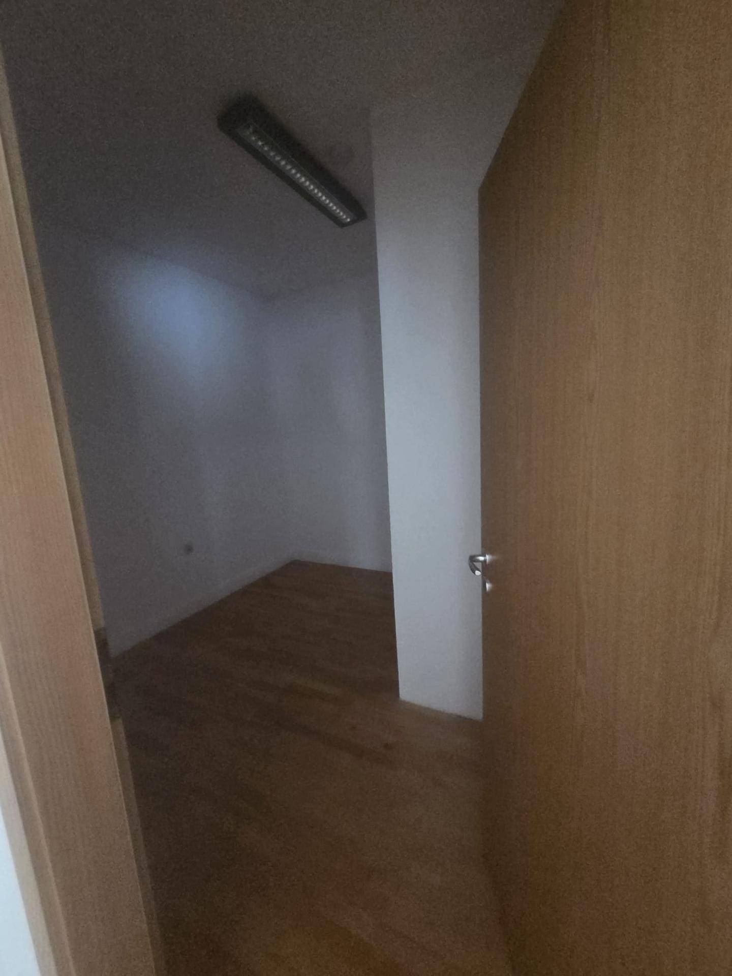 Dunkler, leerer Raum mit Holzboden, durch eine offene Tür sichtbar.