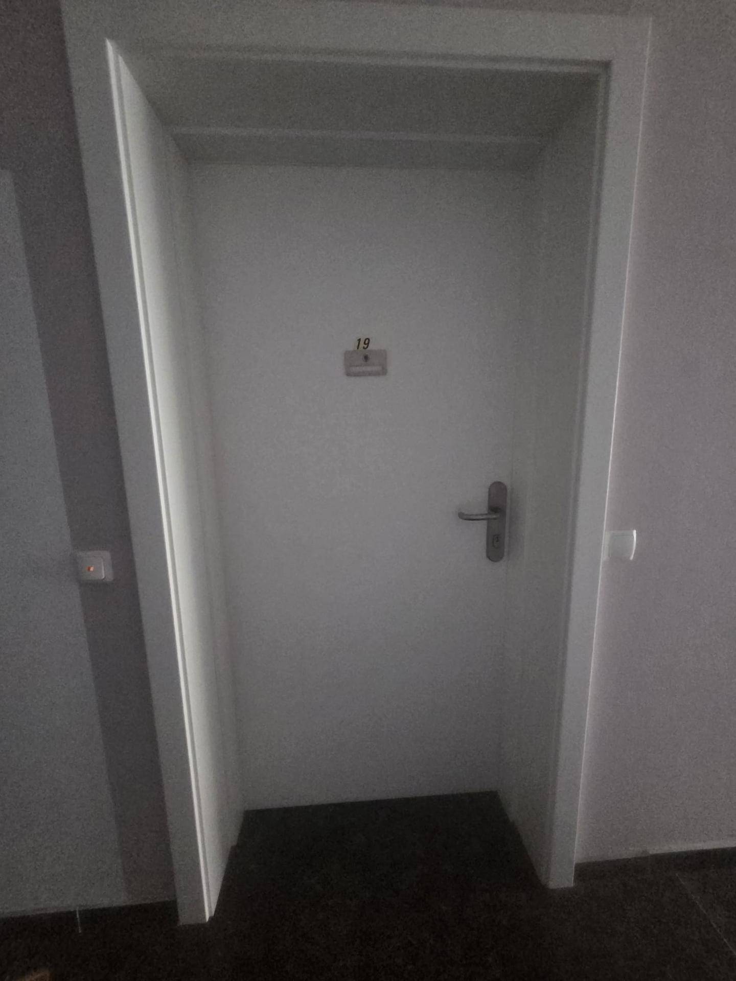 Weiße Wohnungstür mit der Nummer 19 in einem Flur.