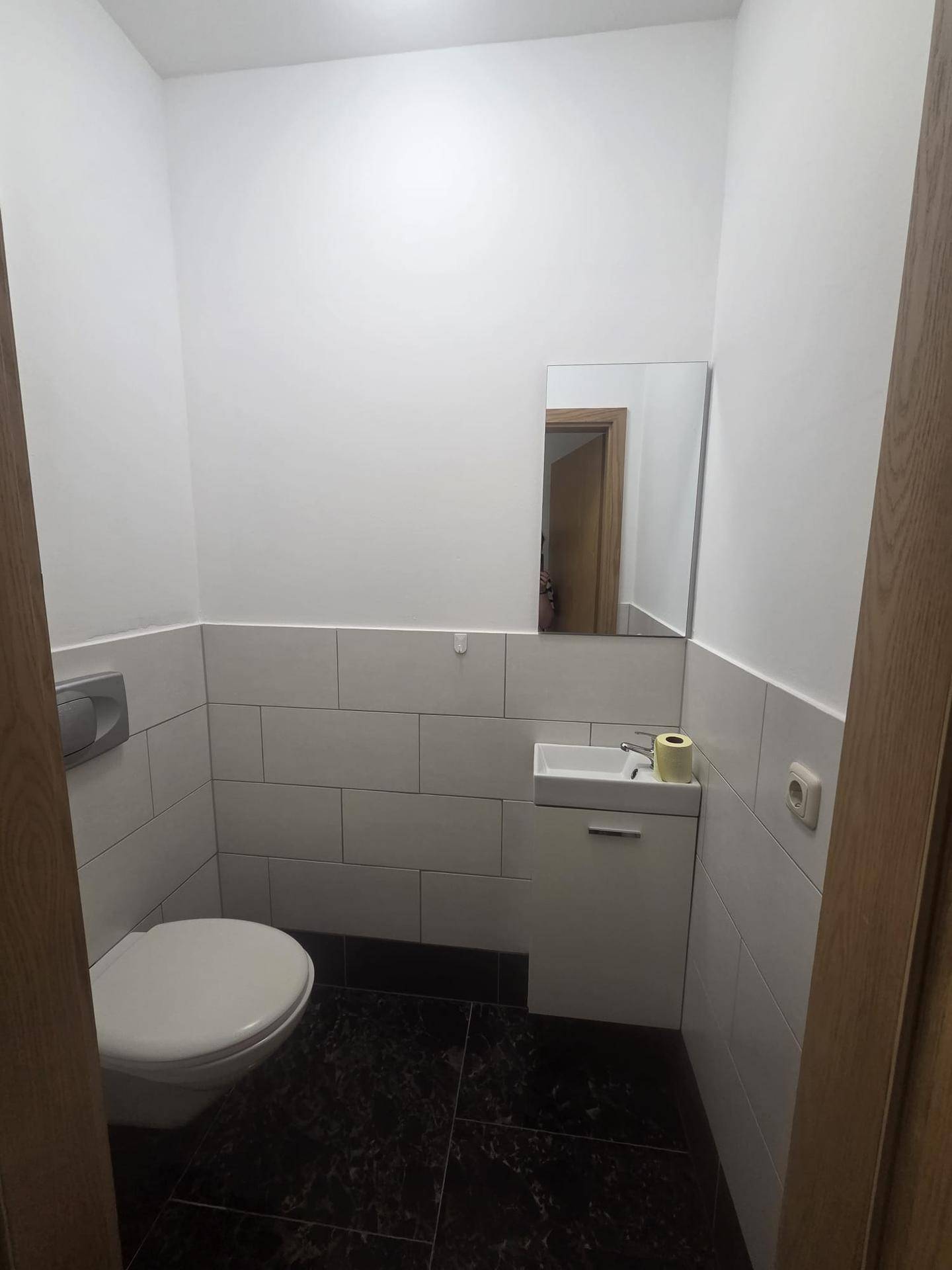 Sauberes Gäste-WC mit weißen Fliesen, wandhängender Toilette und kleinem Waschbecken.