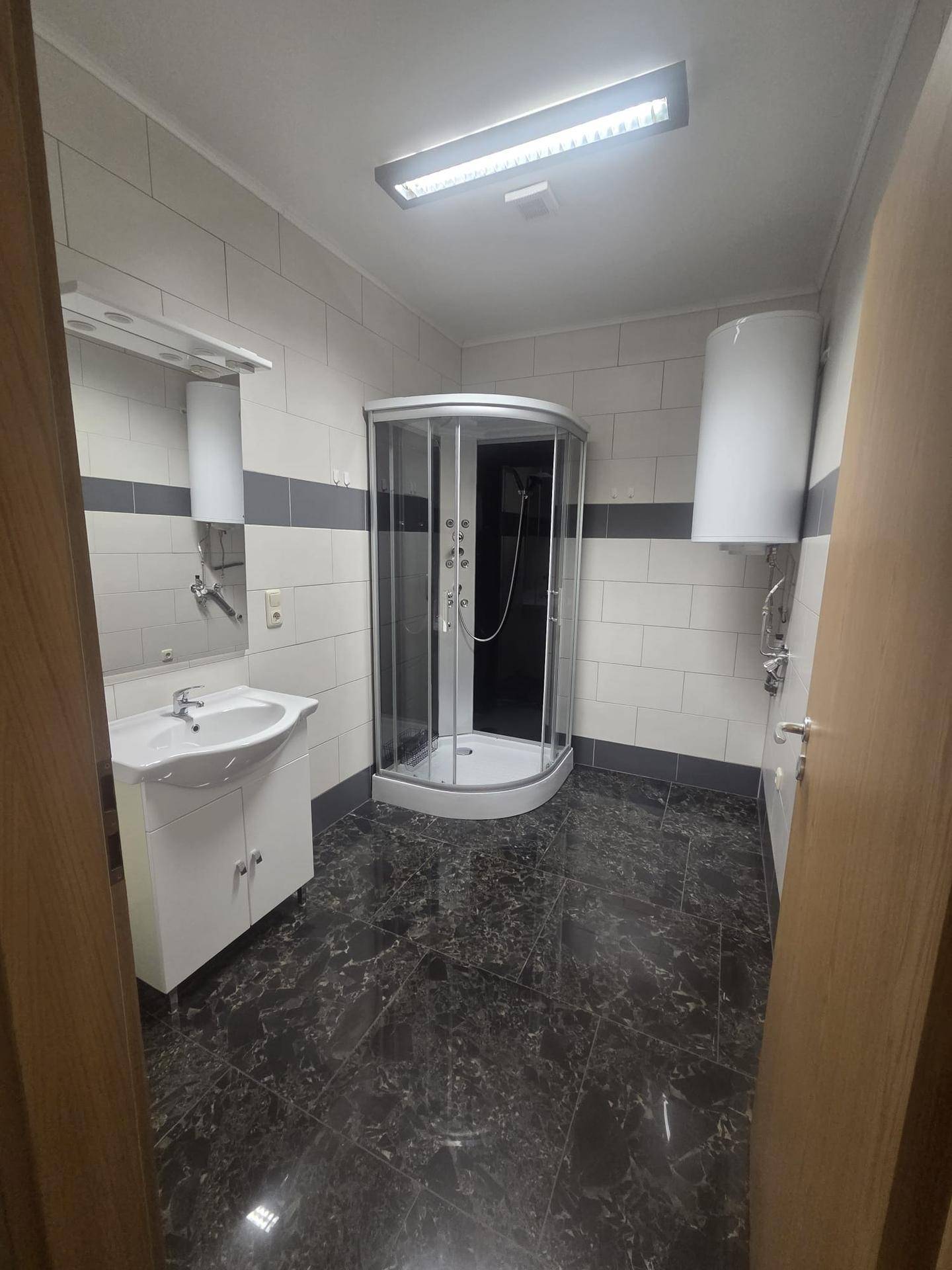Funktionales Badezimmer mit Duschkabine, Waschbecken und großformatigen Fliesen.