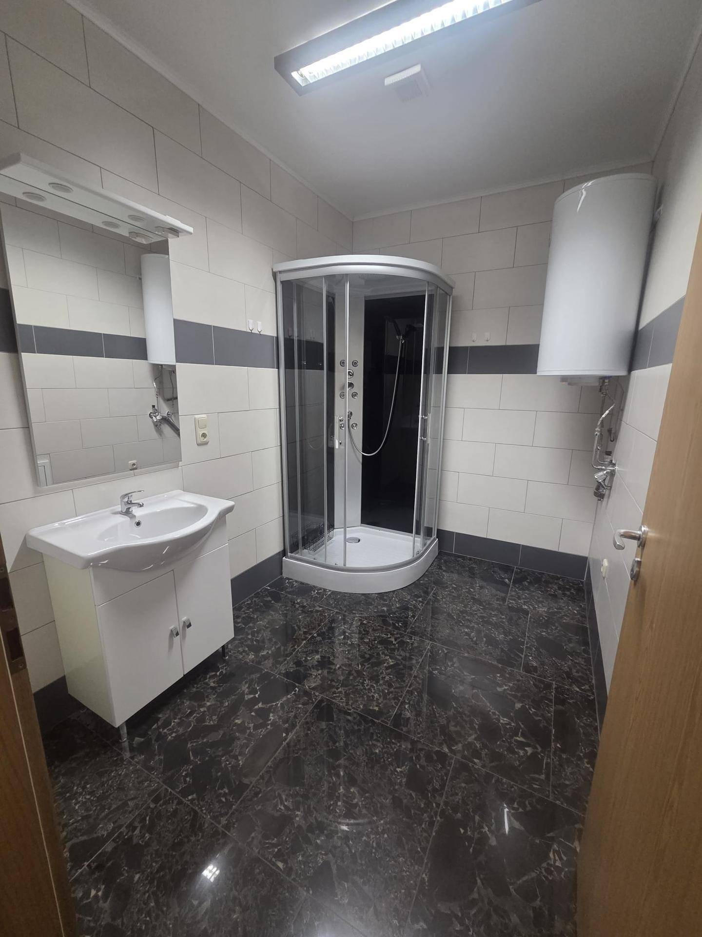 Geräumiges Badezimmer mit Eckduschkabine, Waschbecken und dunklem Fliesenboden.