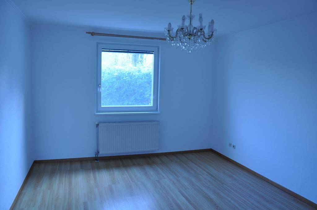 Helles Schlafzimmer mit Laminatboden, großem Fenster und einem Kronleuchter an der Decke.