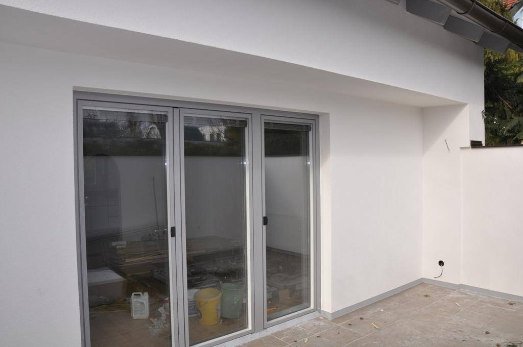 Unfertige Terrasse mit großen Glasschiebetüren, die Zugang zum Innenbereich ermöglichen.
