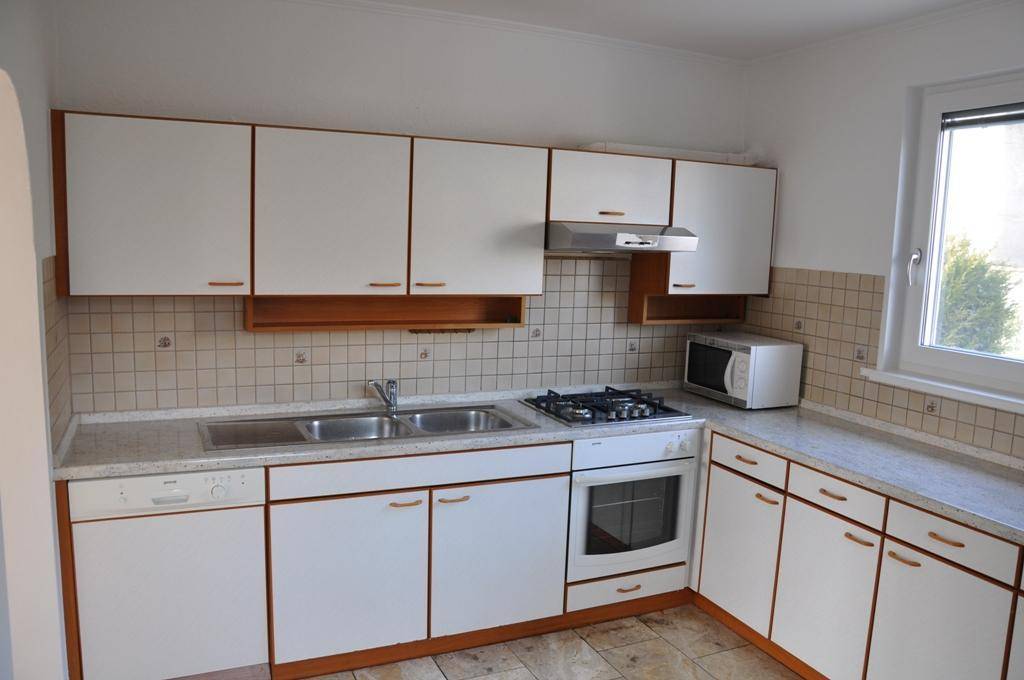 Funktionale Küche mit weißen Schränken, Gasherd, Backofen und Mikrowelle, geflieste Arbeitsplatte.