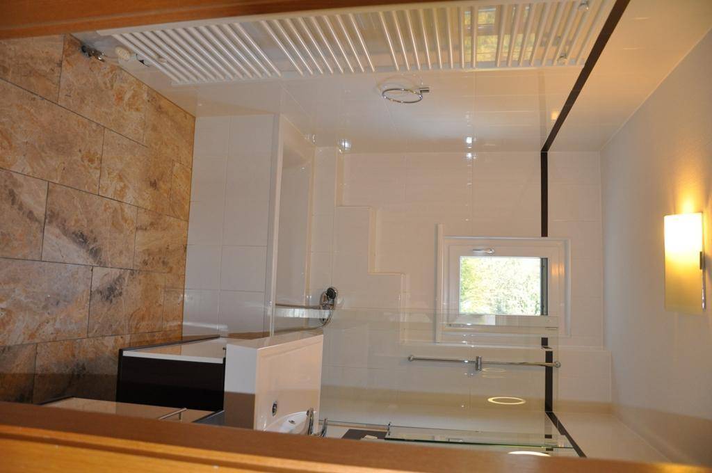 Modernes Badezimmer mit Steinwandfliesen, weißer Einrichtung und begehbarer Dusche.