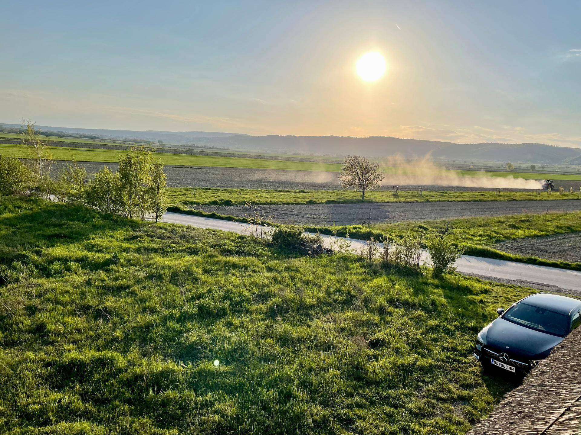 Weitläufiger Blick über grüne Felder und sanfte Hügel unter einem strahlenden Sonnenuntergang.