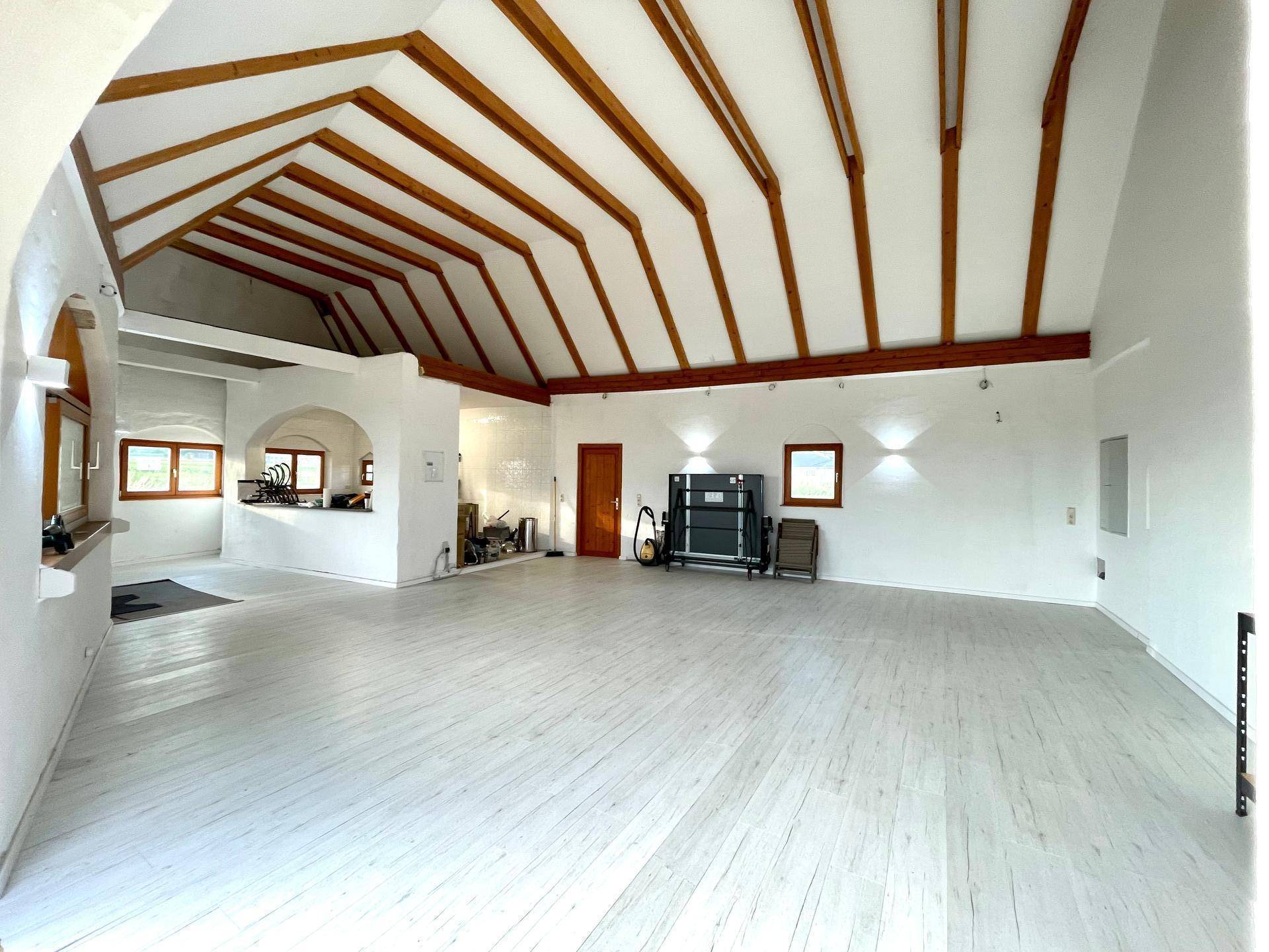 Weitläufiger Innenbereich mit markanten Holzbalken und weißem Boden, der eine moderne und offene Atmosphäre schafft.