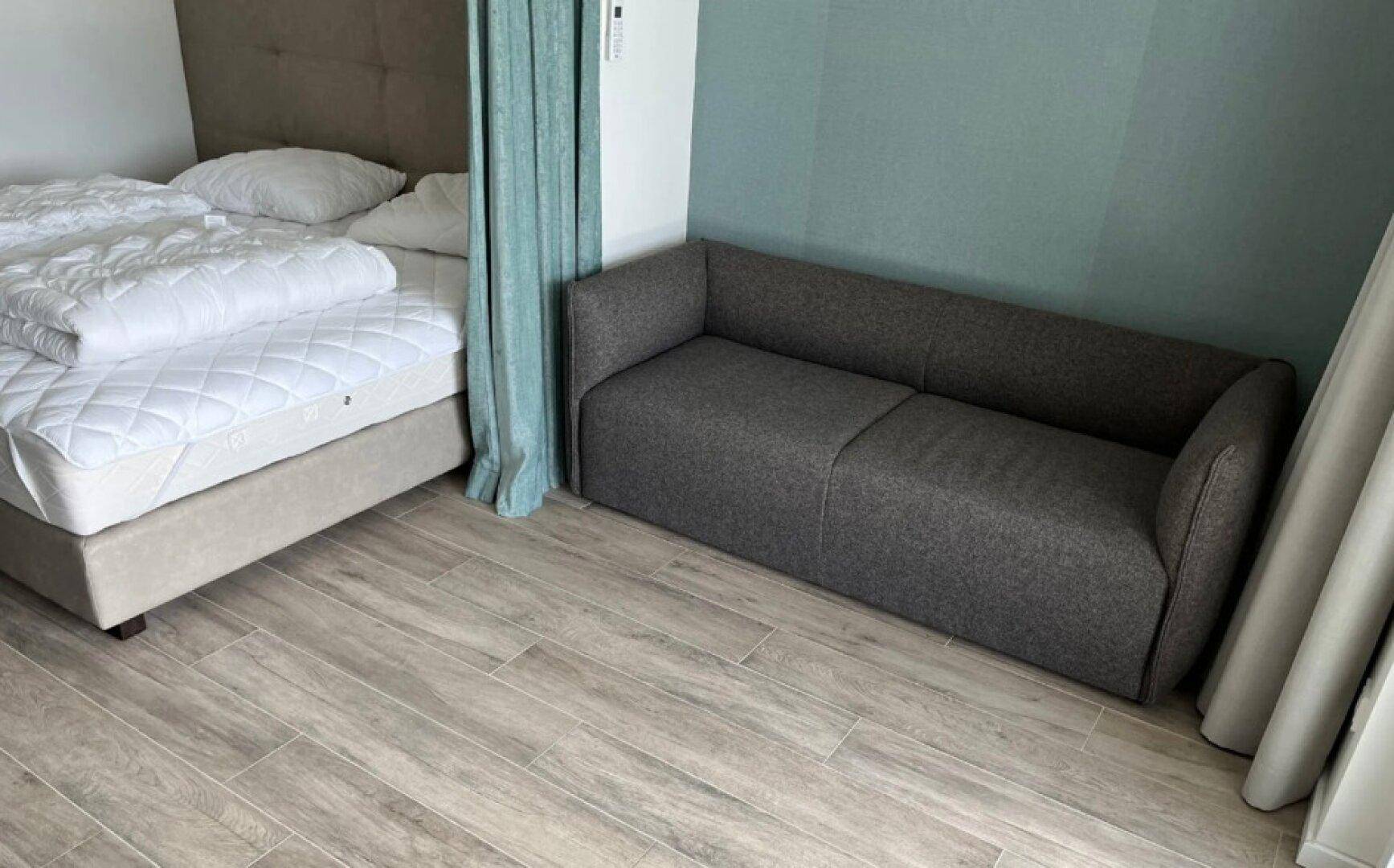 Kombinierter Wohn- und Schlafbereich mit bequemem Sofa und modernem Bodenbelag.