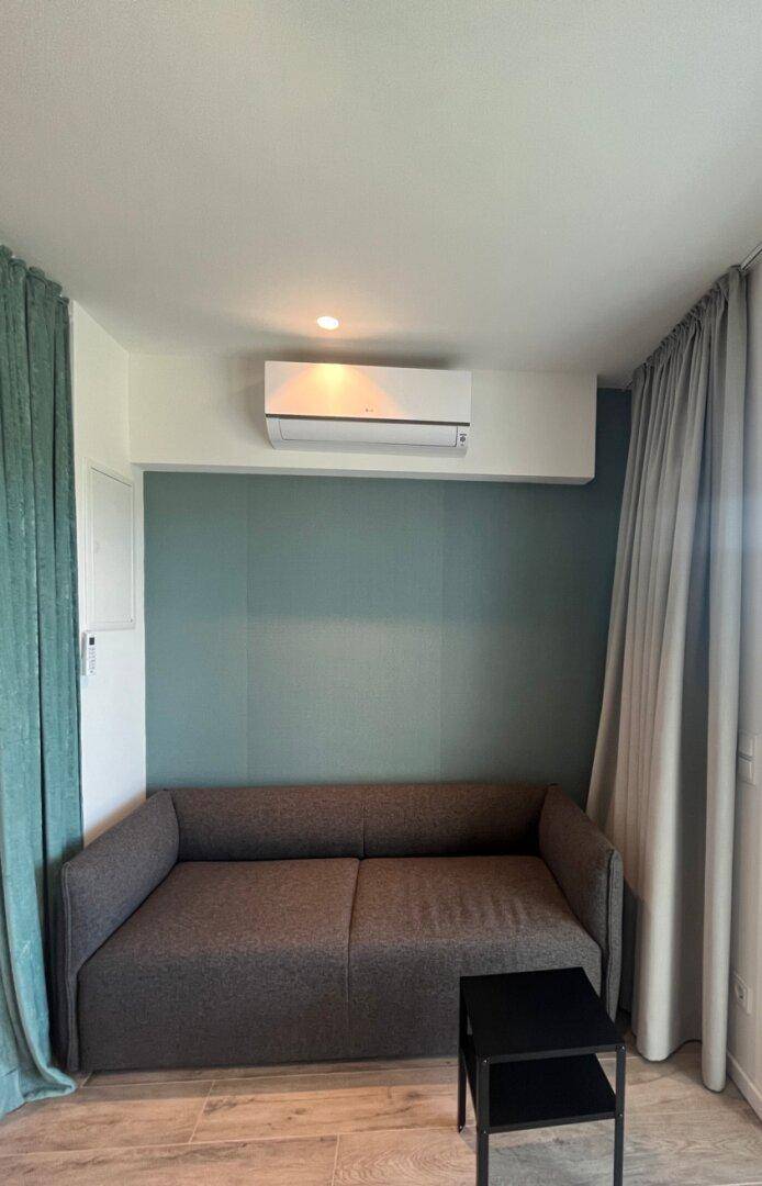 Gemütlicher Wohnbereich mit Sofa, Klimaanlage und farbiger Akzentwand.