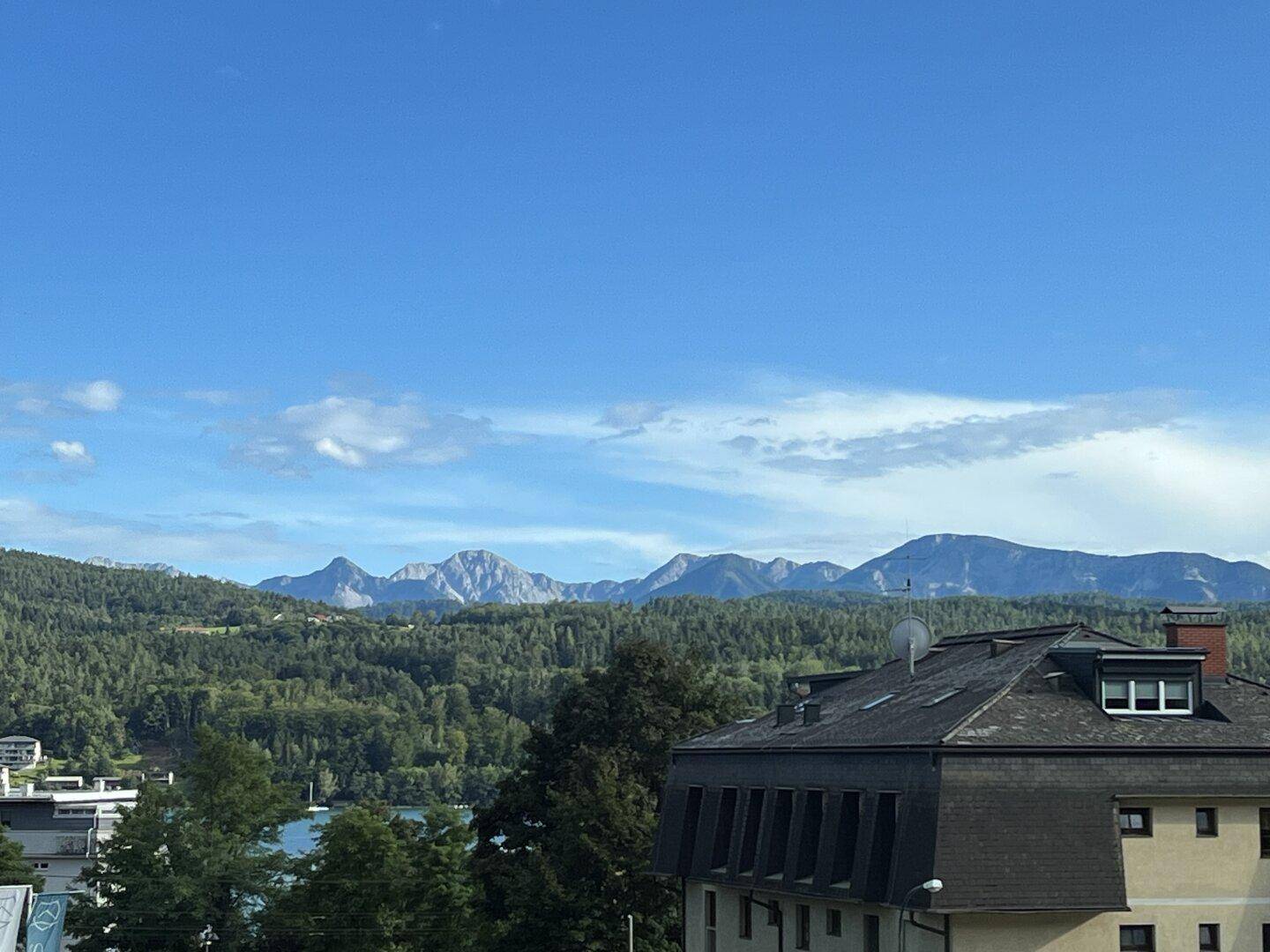 Panoramablick auf die umliegende Berglandschaft und einen See unter blauem Himmel.