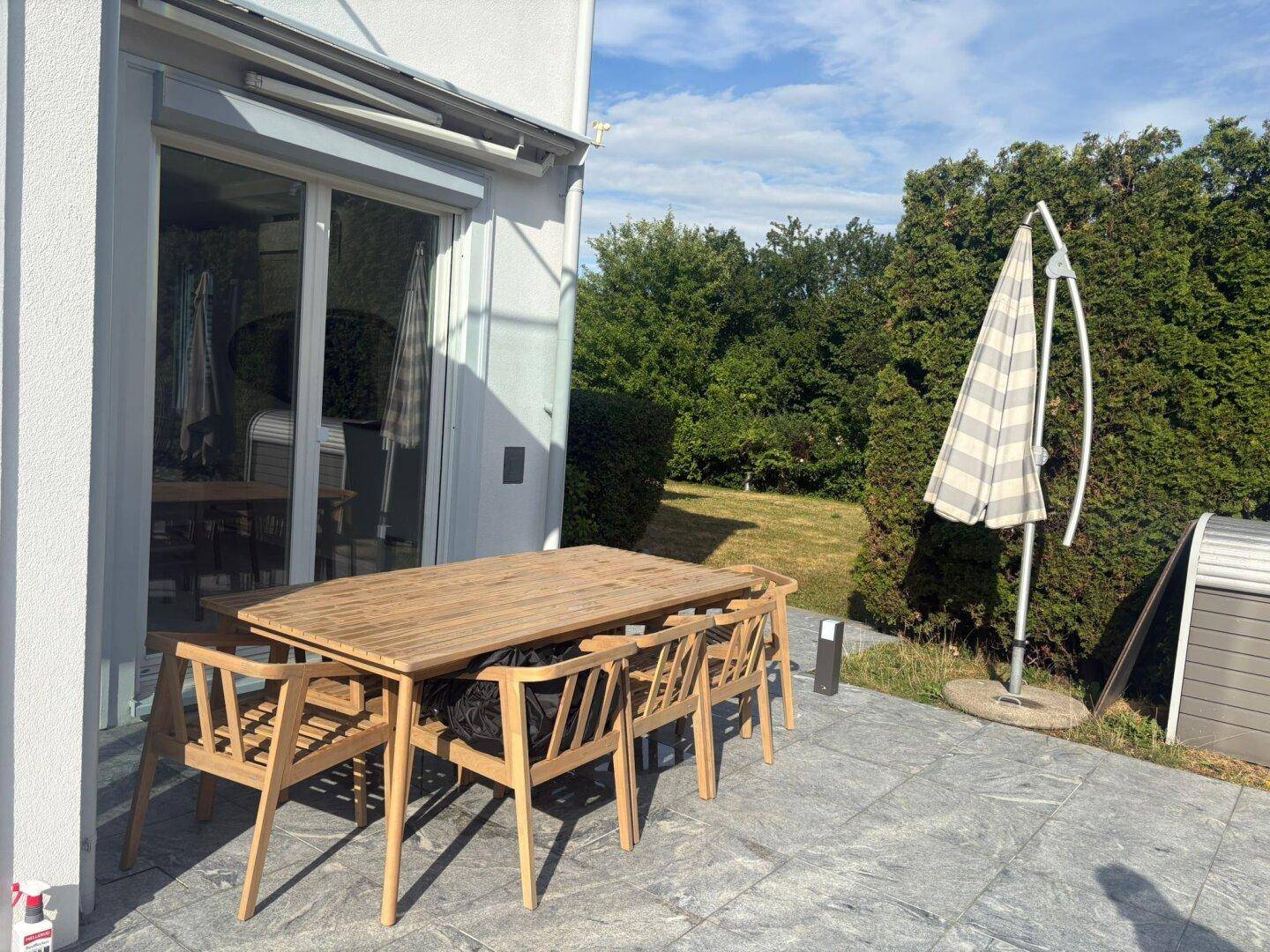 Gepflasterte Terrasse mit Holztisch und Stühlen, ideal für Mahlzeiten im Freien mit Gartenblick.
