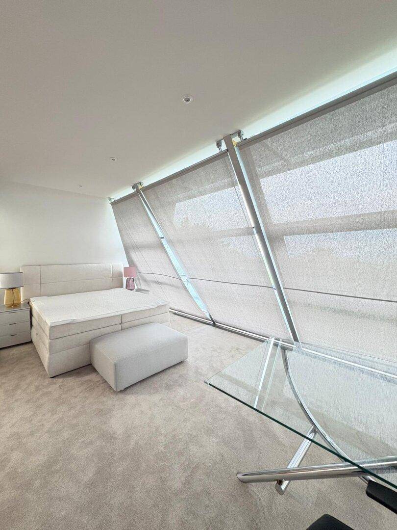 Modernes Schlafzimmer mit großen schrägen Fenstern, Teppichboden und komfortablem Bett.