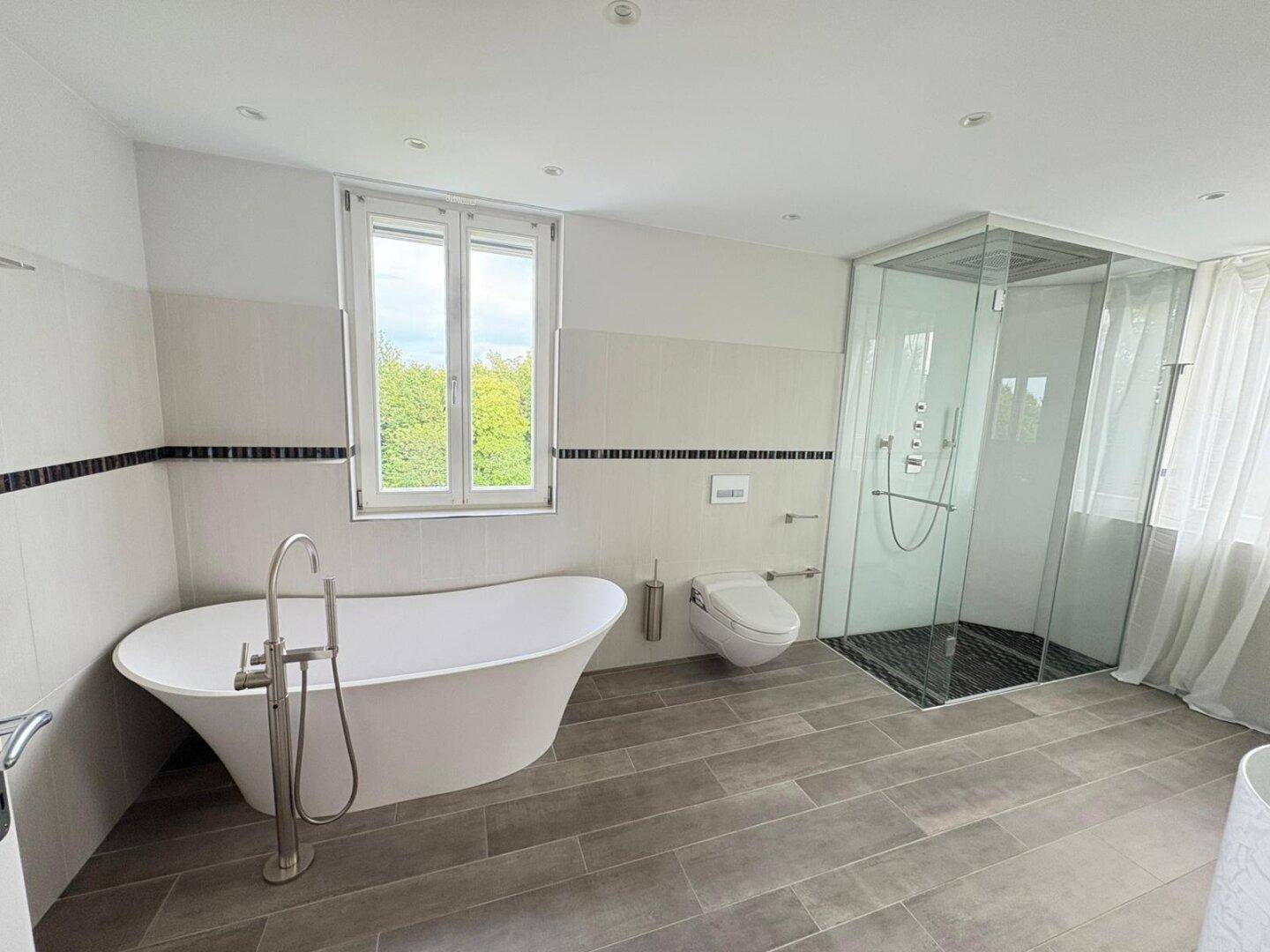Modernes Badezimmer mit freistehender Badewanne, begehbarer Dusche und Fenster.