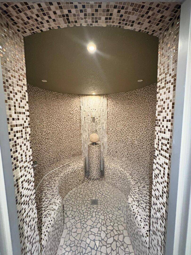 Luxuriöser Dampfbadbereich mit Mosaikfliesen und geschwungenen Sitzgelegenheiten.