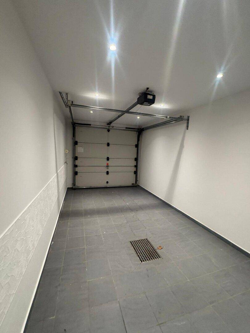 Saubere und leere Garage mit automatischem Garagentor und Fliesenboden.