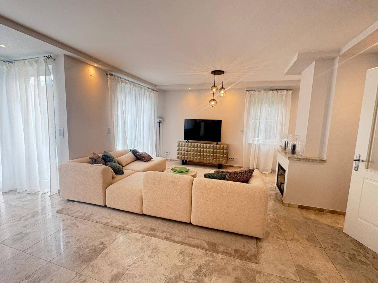 Geräumiges Wohnzimmer mit modernem Sofa, Kamin und großen Fenstern zum Garten.
