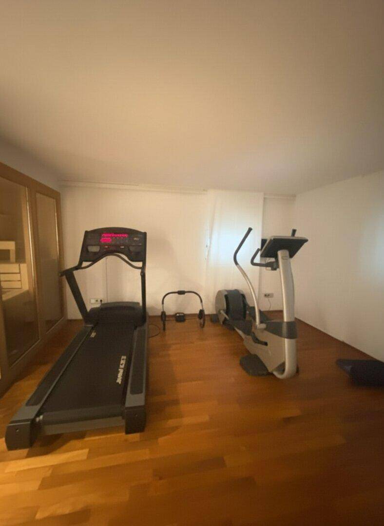 Privater Fitnessraum mit Laufband und Crosstrainer auf einem Holzfußboden.