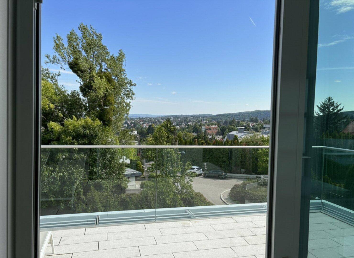 Moderne Terrasse mit Glasgeländer und weitem Blick über die grüne Umgebung.