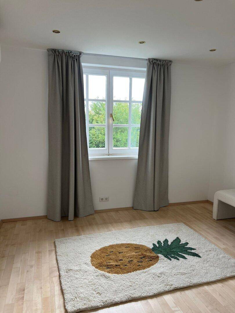 Helles Schlafzimmer mit Holzboden, großem Fenster und einem dekorativen Teppich.