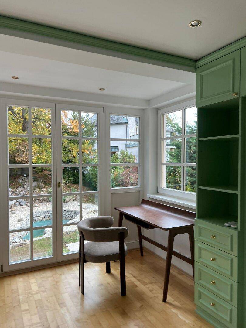 Helles Arbeitszimmer mit Holzboden, grünem Einbauschrank und Blick in den Garten.