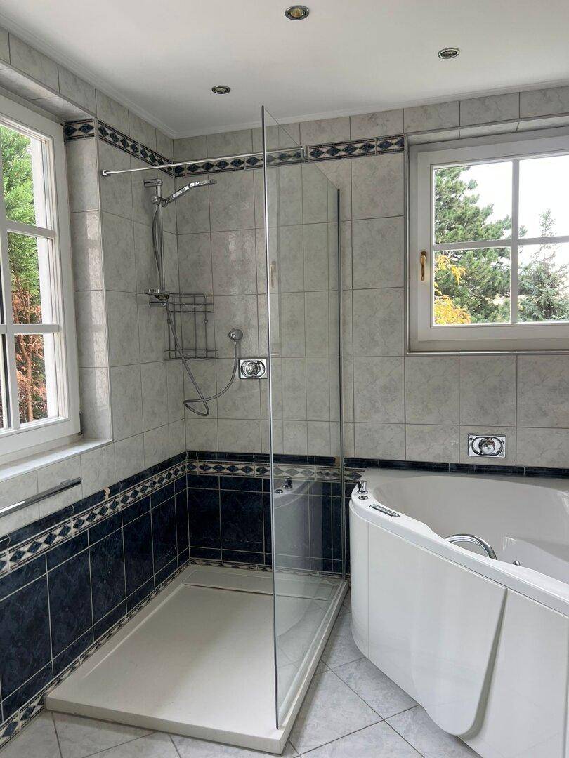 Modernes Badezimmer mit Dusche, Eckbadewanne und zwei Fenstern für viel Tageslicht.