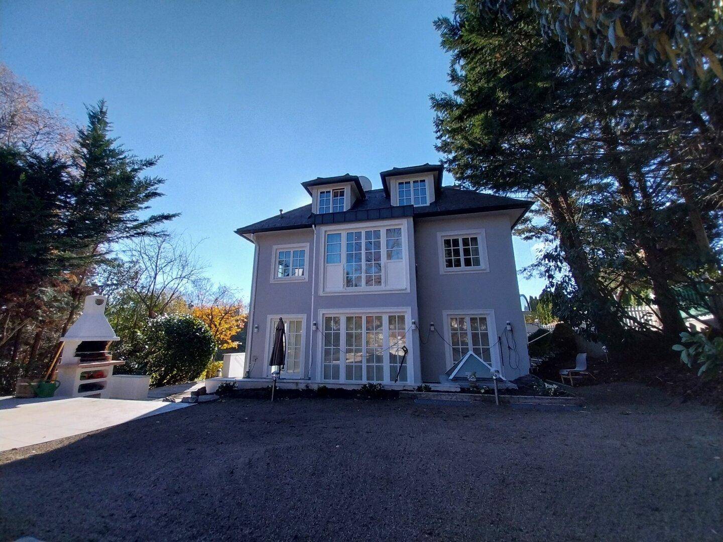 Rückansicht der Villa mit weitläufigem Garten und viel Grünfläche unter blauem Himmel.