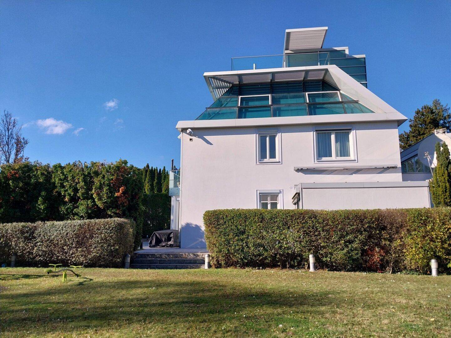 Seitenansicht der modernen Villa mit grünen Hecken und klarem blauem Himmel.