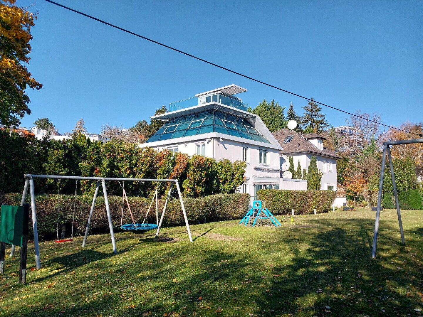 Gartenbereich mit Kinderspielplatz und der modernen Villa im Hintergrund.