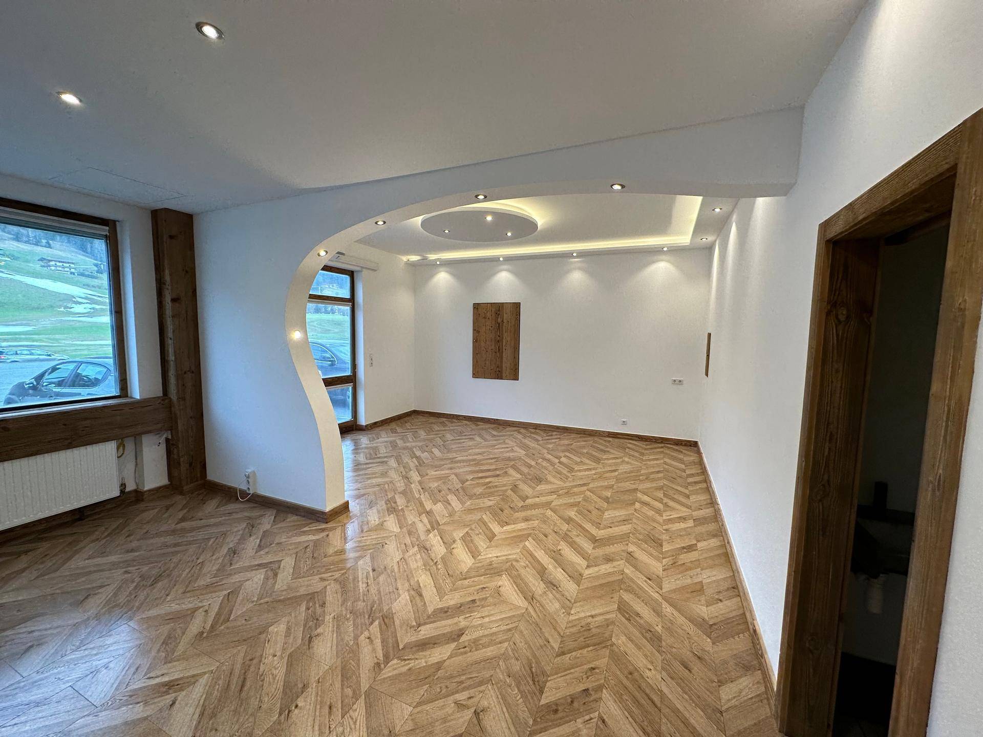 Geräumiger Wohnbereich mit elegantem Parkettboden, weißen Wänden und moderner Deckenbeleuchtung.