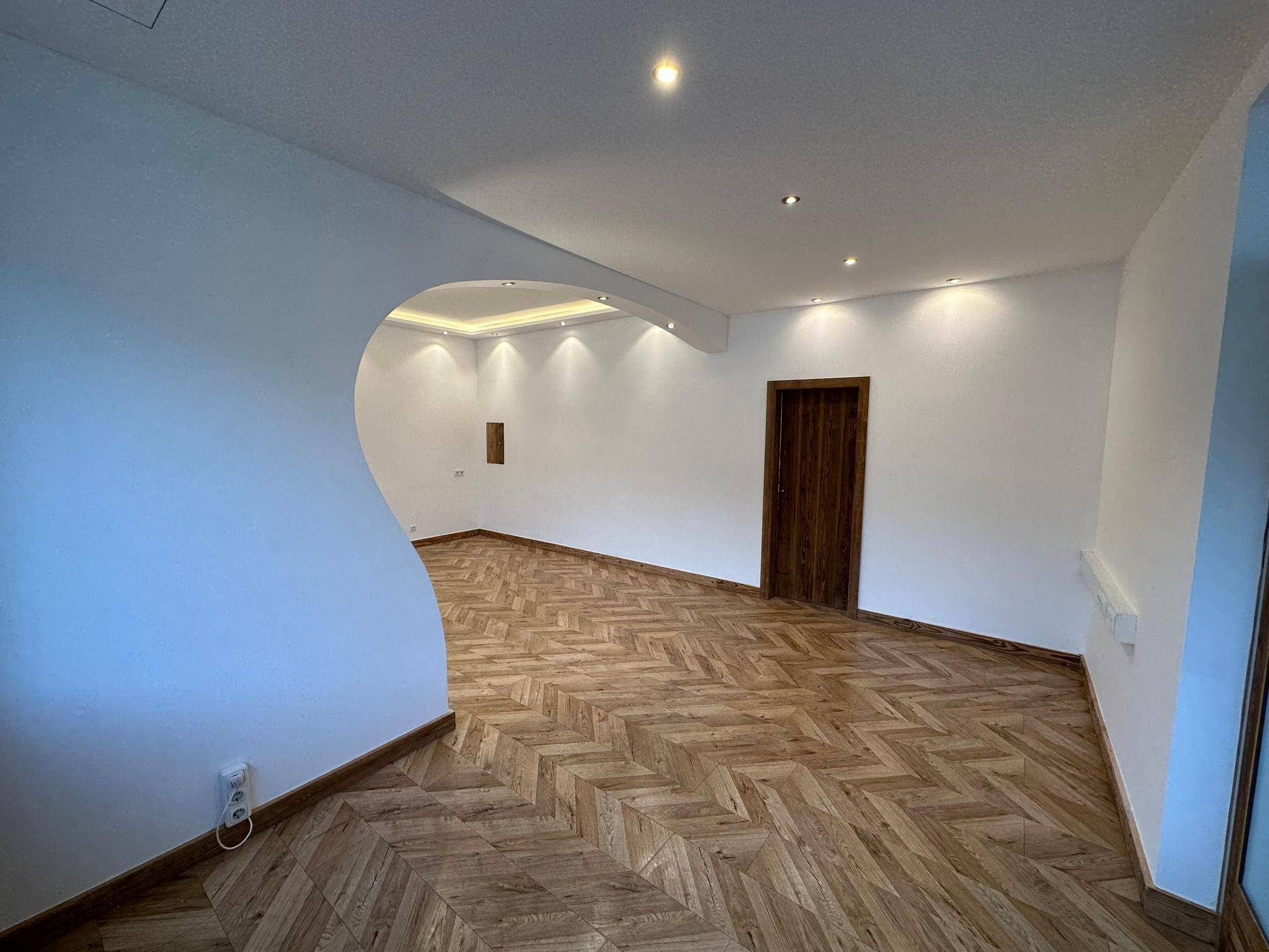 Heller, leerer Wohnraum mit ansprechendem Parkettboden und indirekter Beleuchtung an der Decke.