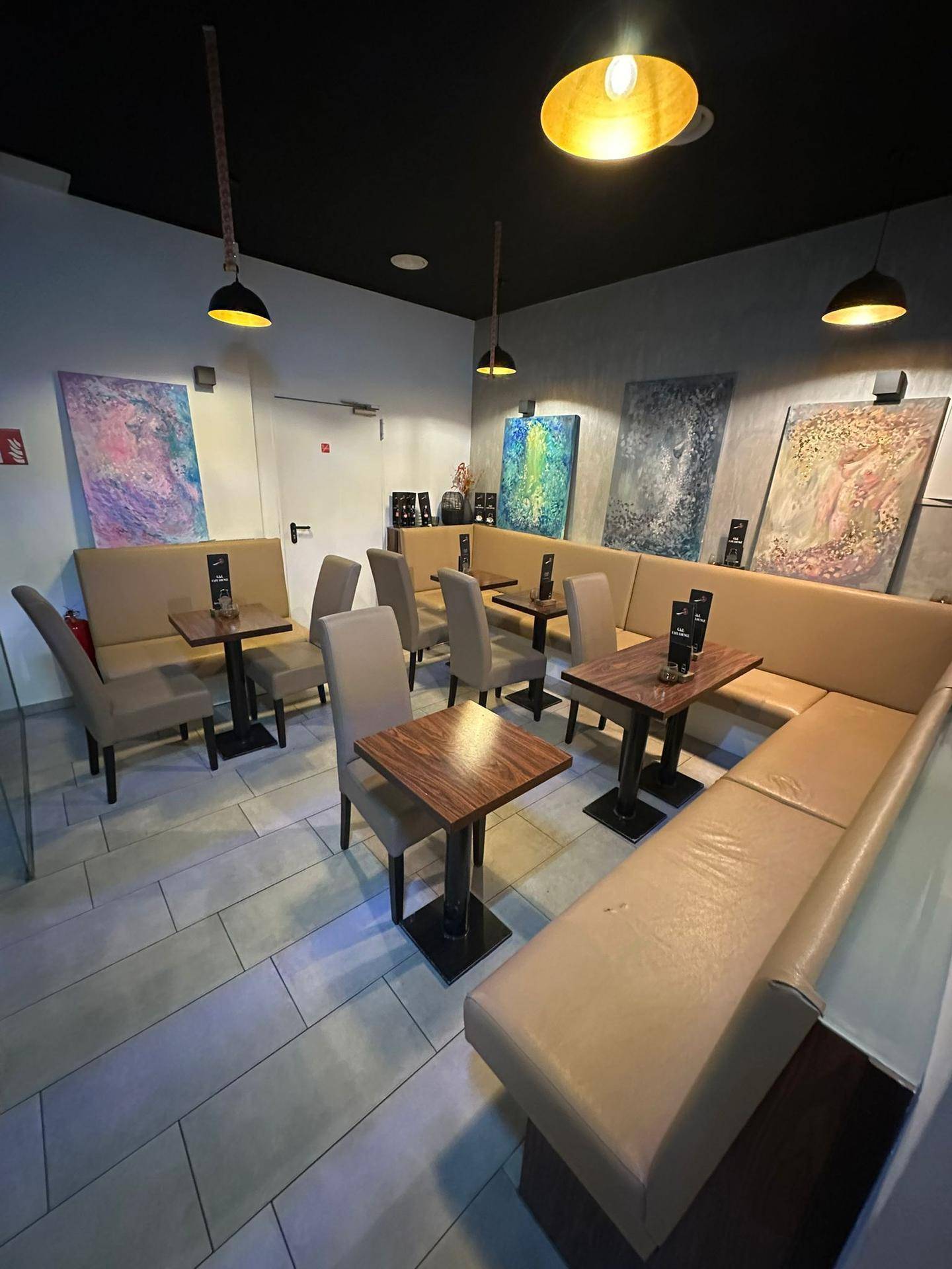 Gemütlicher Sitzbereich der Café-Lounge mit gepolsterten Bänken, Tischen und farbenfrohen Kunstwerken an den Wänden.