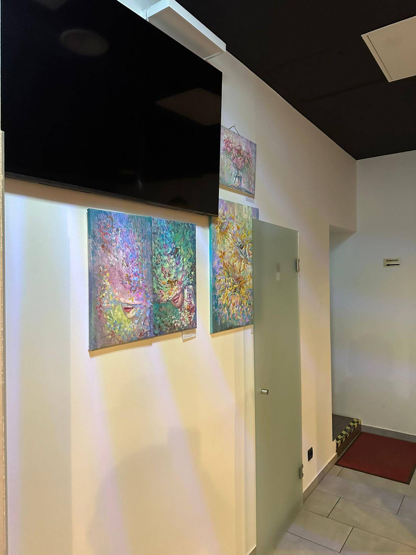 Wandbereich in der Lounge mit farbenfrohen Kunstwerken, einem Wandfernseher und einer Glastür.