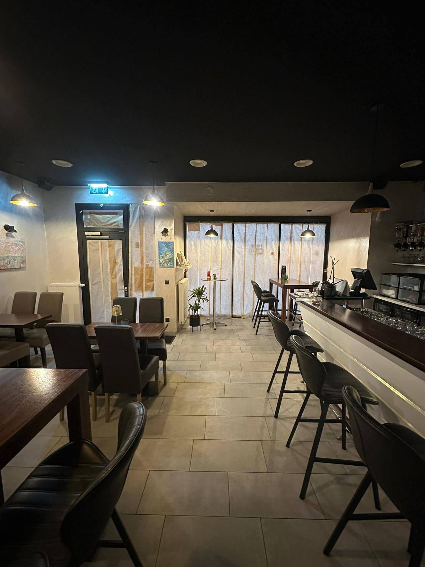 Geräumiger Innenbereich der Café-Lounge mit verschiedenen Tischen, Stühlen und der Bar im Hintergrund.