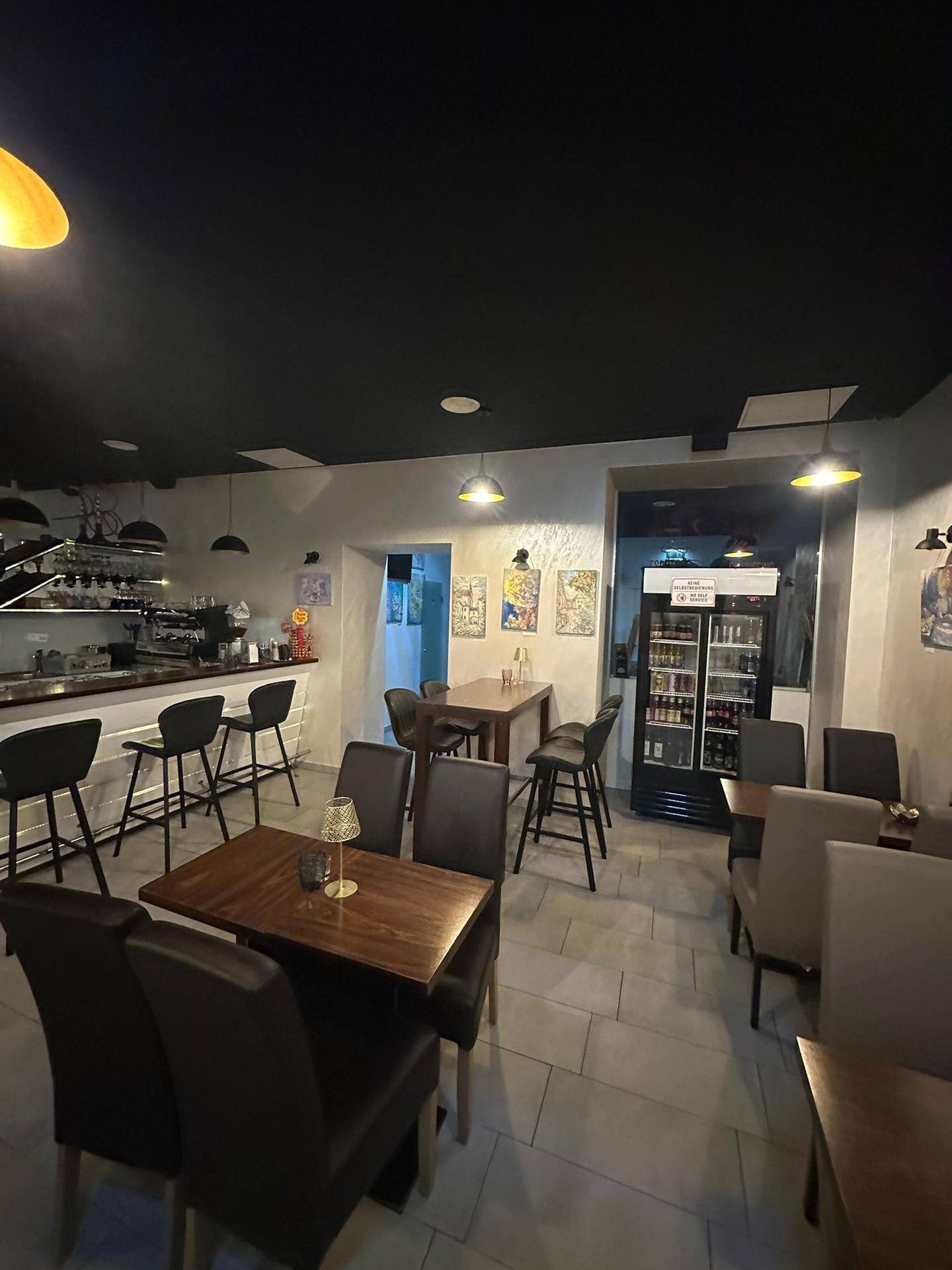Übersicht über die Café-Lounge mit Bar, verschiedenen Sitzbereichen und einem Getränkekühlschrank.