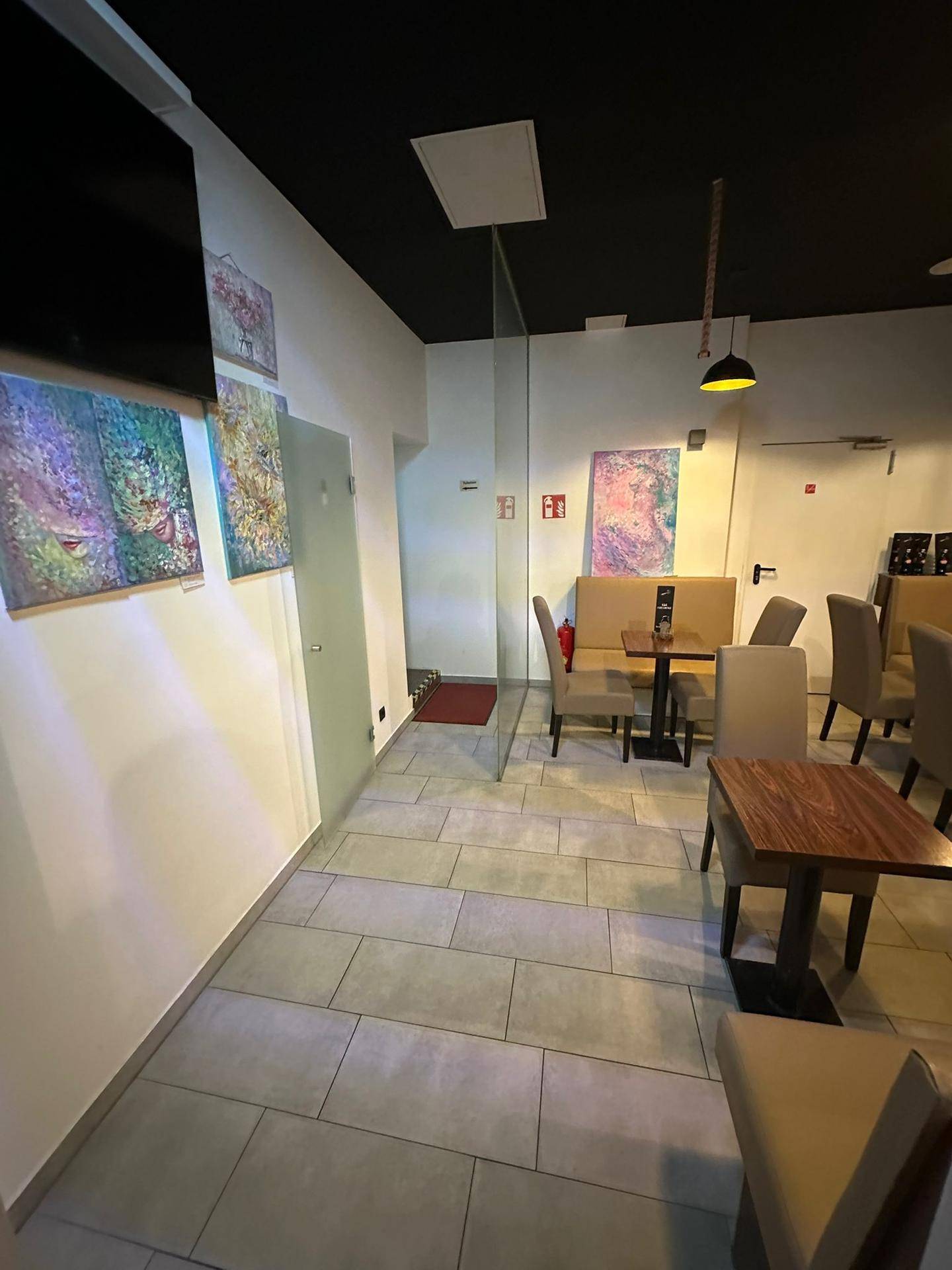 Blick in den hinteren Bereich der Café-Lounge mit Sitzgelegenheiten, Kunstwerken und einer Glastrennwand.