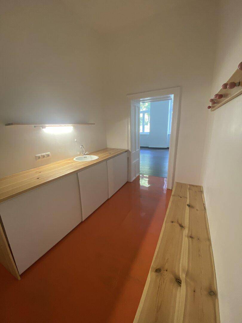 Langer Raum mit orangefarbenem Boden, Holzarbeitsplatte mit Spüle und Zugang zu einem weiteren Zimmer.