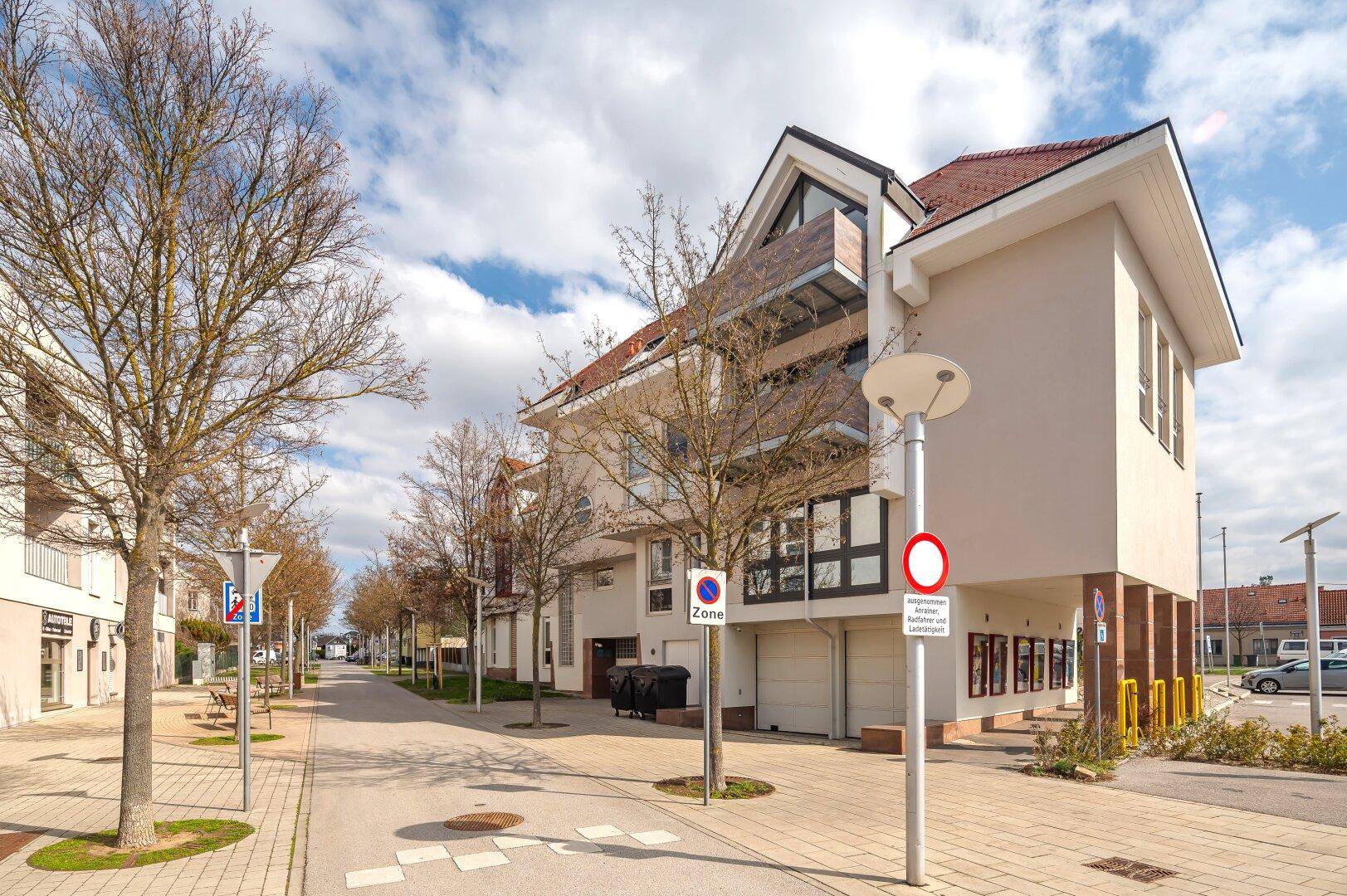 Moderne Wohnanlage mit Balkonen, Garagen und gepflegter Straßenansicht unter blauem Himmel.